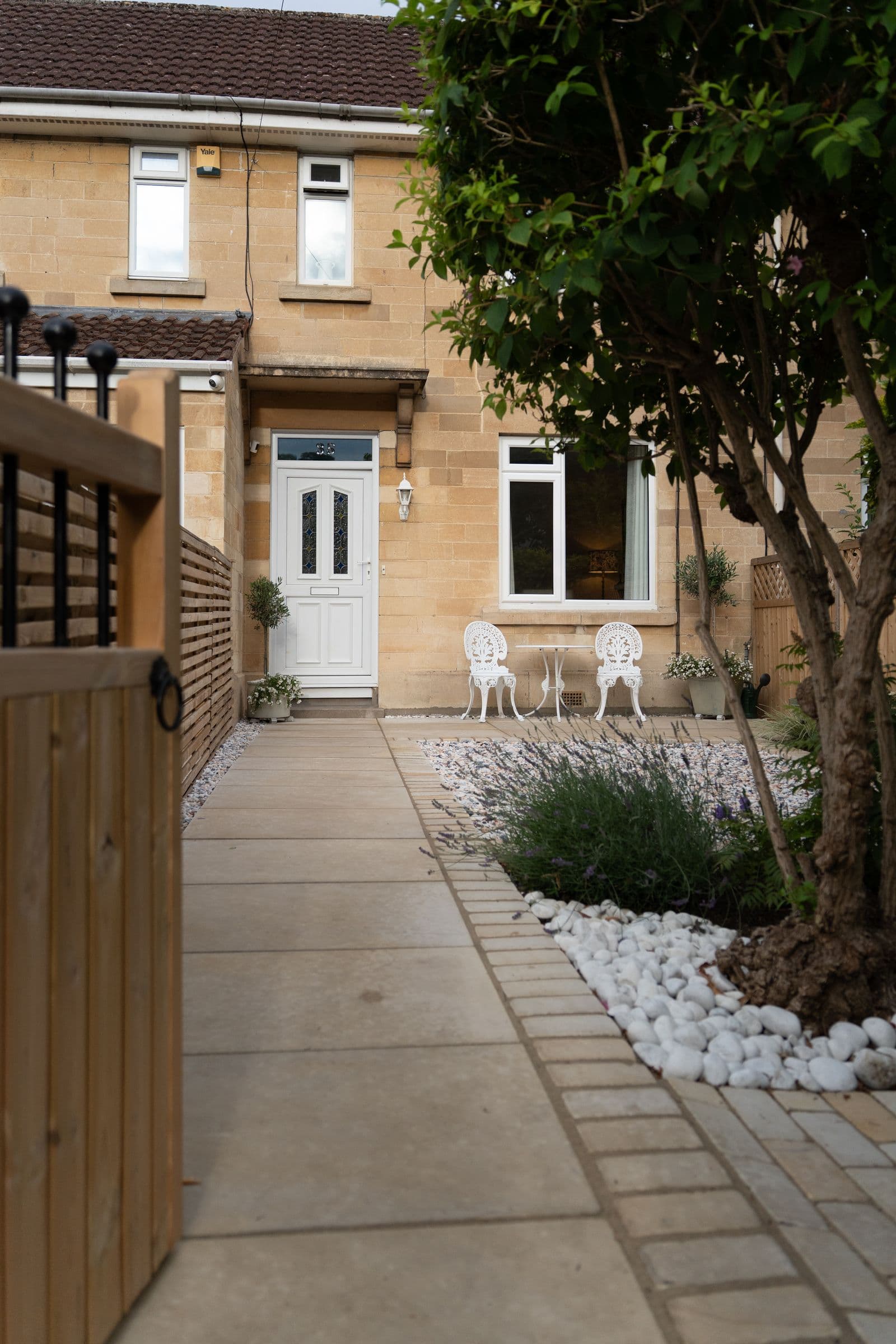 The paved path along the front garden, past the tree and the white stone border.
