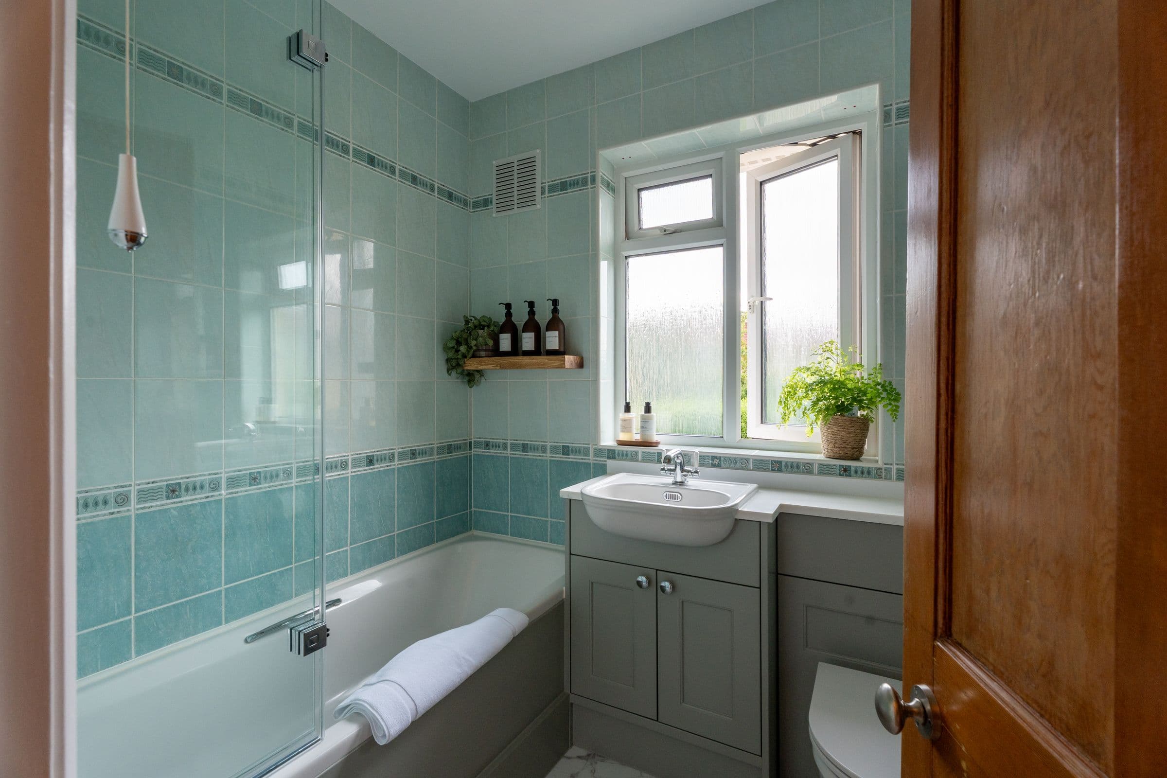 The bathroom, with the bath and shower over, green tiling and the window.
