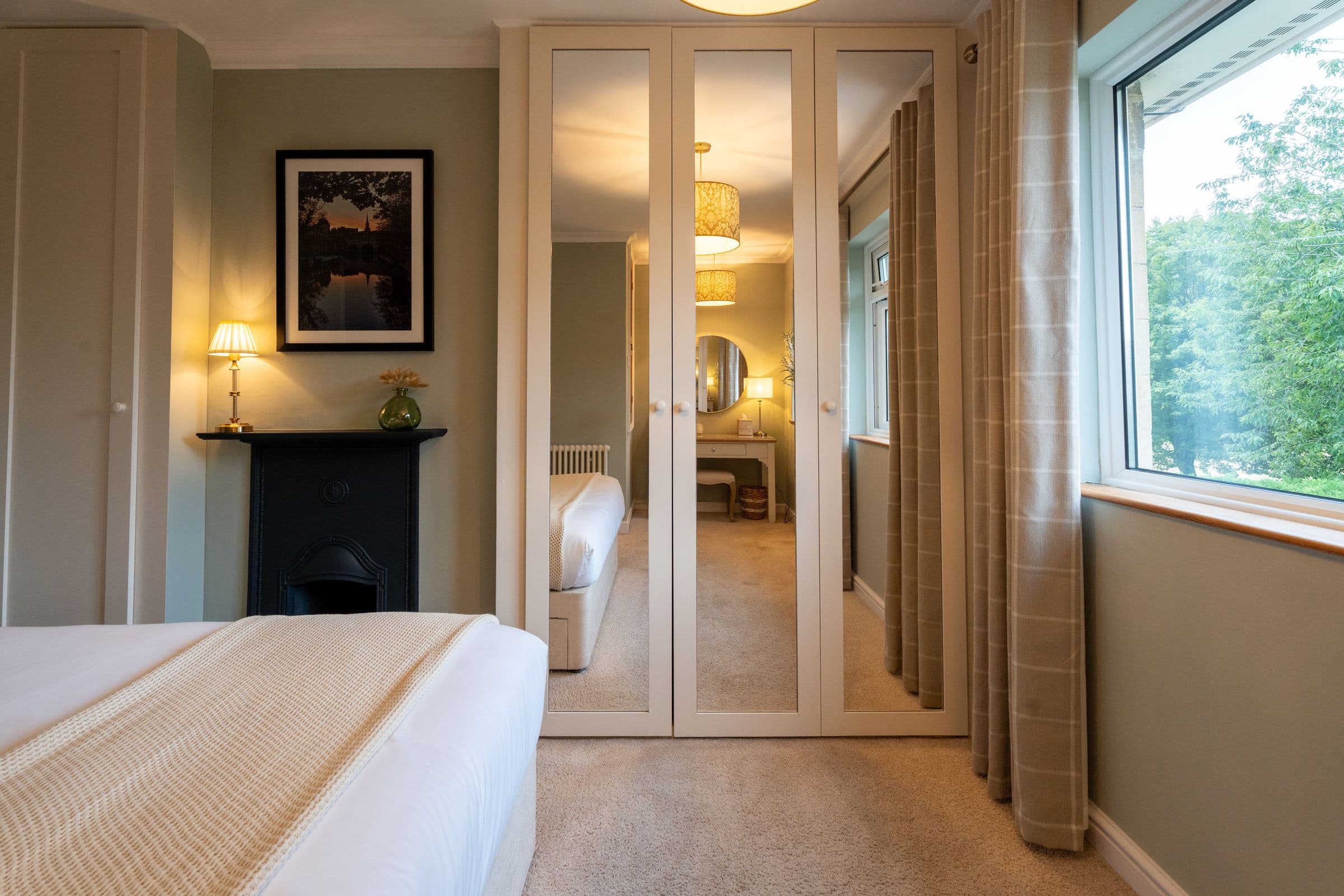 The main bedroom reflected in the mirrored wardrobes, with the window beyond.