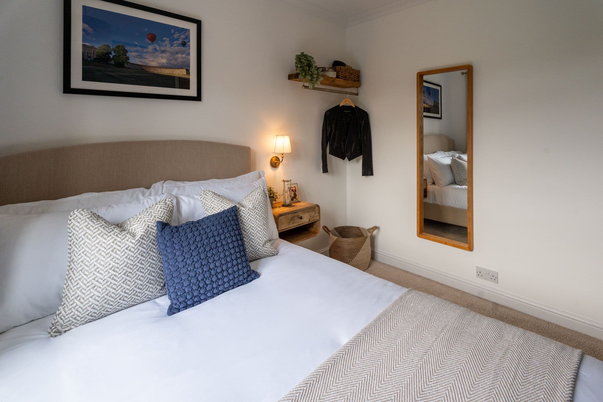 The second bedroom's bed, dressed in white cotton with woven and blue cushions.