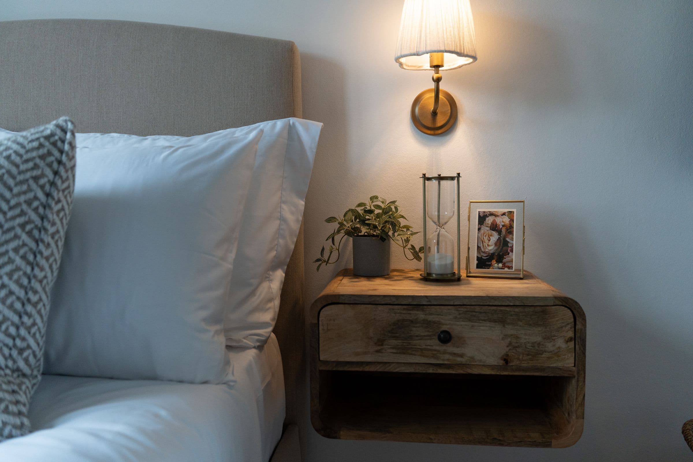 The floating bedside shelf with its hourglass, plant and framed photograph.