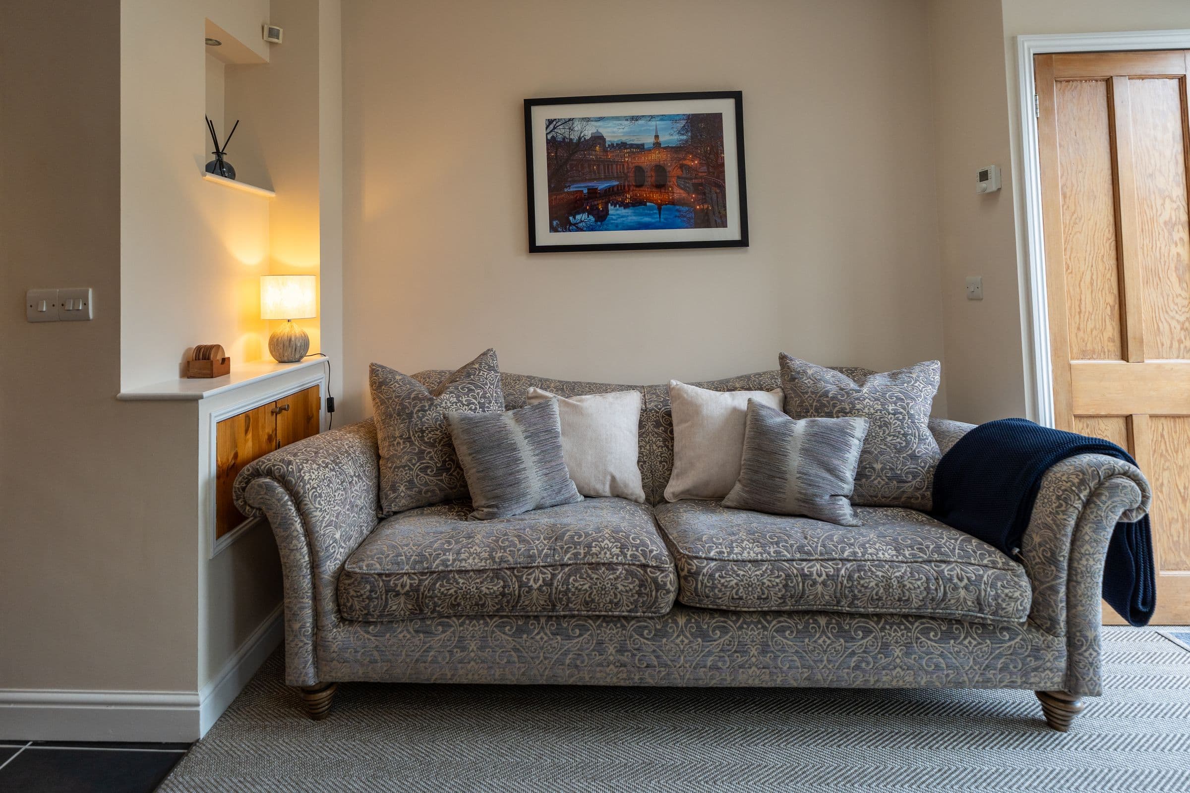 The garden room sofa, plumped with cushions under the lamp.