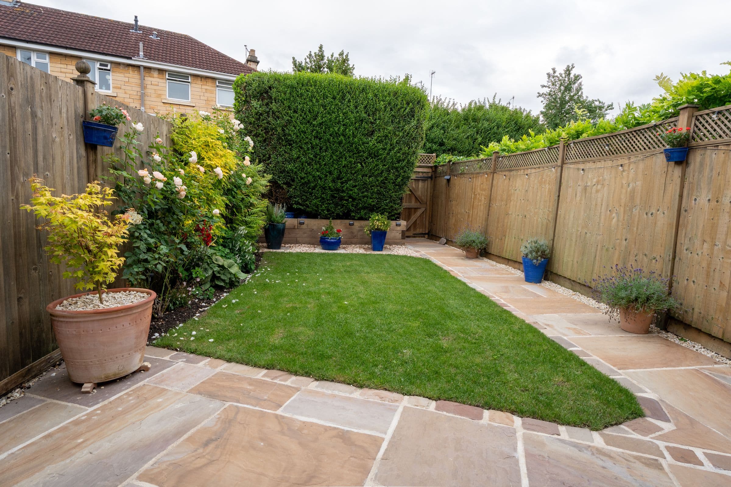 The enclosed rear garden — lawn, paved path and planted borders inside the high fence.