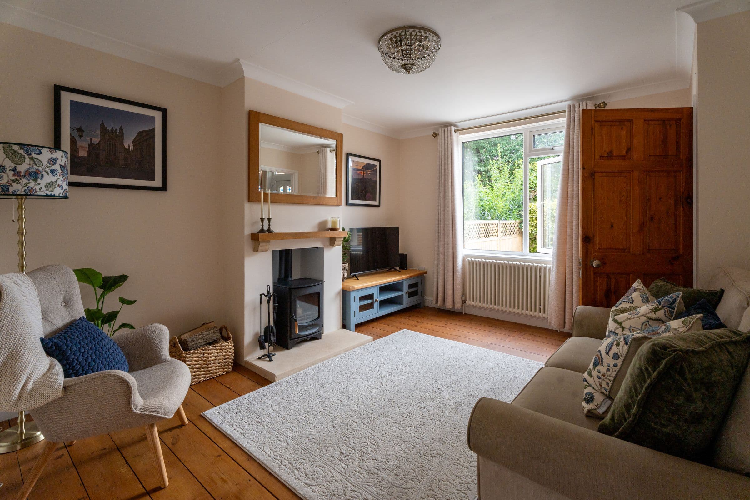 The living room from the doorway — armchair, wood burner and sofa around the rug.